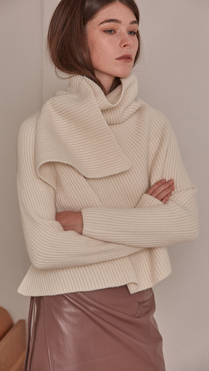 Cecil Sweater, a knit sweater in cream ivory. Rollback collar with pointed wide cowl neck. Drop shoulder design, open rib details. Short length in open back.