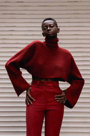 The Gianni sweater in burgundy featuring bell sleeves and cropped hemlines. Ribbed knit from soft, thick wool fits neatly on the shoulder and cuffs but is exaggerated through the arms and chest. It hits just above the bust. Pull on. Relaxed silhouette