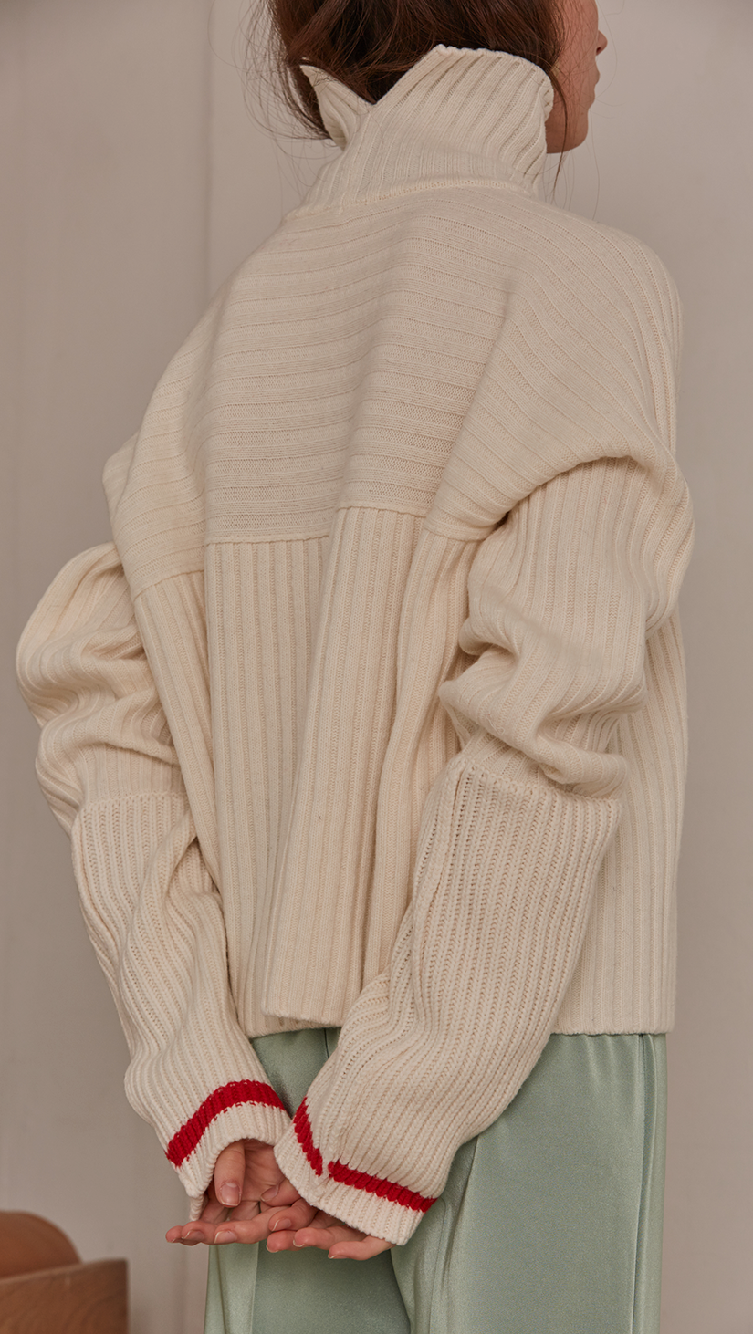   Jupe Sweater in Ivory. Cowl neck ribbed sweater with pointed dropped shoulder seams and extra long raglan sleeves. Designed to be loose fit.
