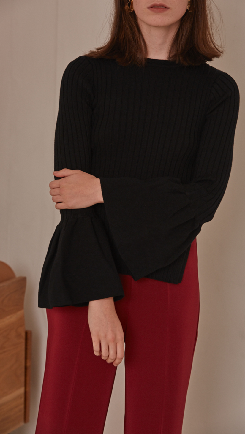 Etre Sweater in Black. Long bell sleeved rib knit in the avant-grade silhouette. Voluminous bell sleeves in cropped length top with side slit. Rounded hem. Super soft feel. Designed to skim the body.