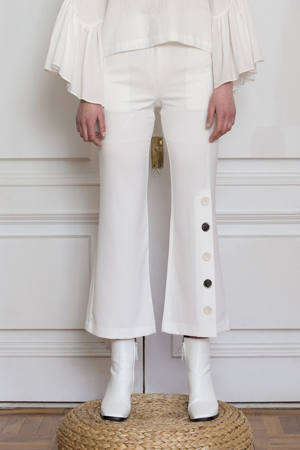 The Adalyn Pant in White featuring on-seam zip fly and hook closure, slanted front pockets, decorative button detail down left side. Partially lined. Cropped silhouette. 