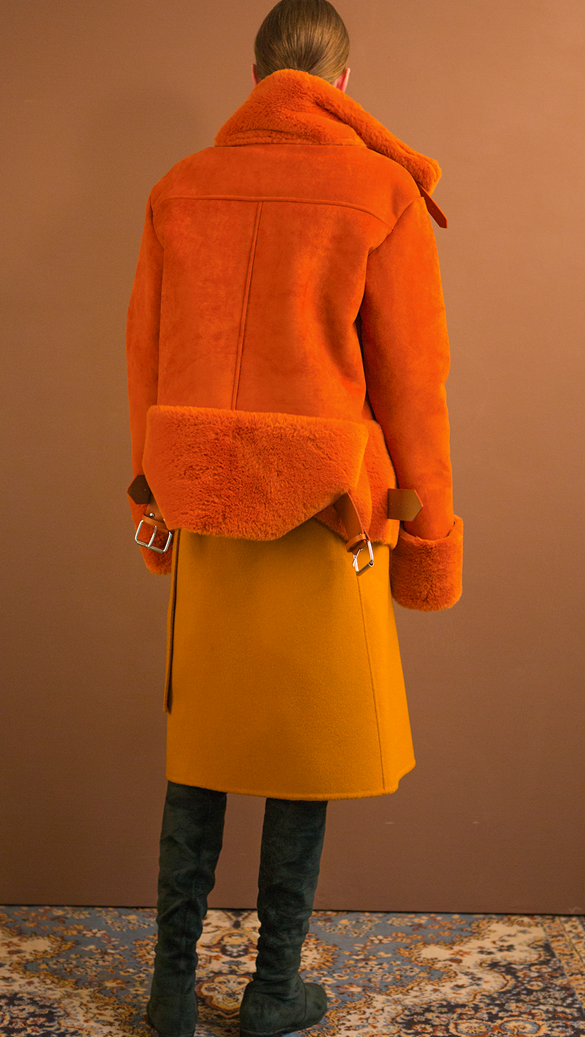 Moto-style suede shearling jacket fully lined in orange shearling. Super soft in suede, dropped shoulder, extra long sleeves with soft shearling detail at cuffs, front zip pockets, gusseted back panel, belt at waist with bucket closure, zip closure with attached wide belt in belt loops, Medium-weight. Fully lined. Oversized. Relaxed silhouette.