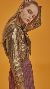 The Blaine is a button-down blouse in glitter gold metallic. With a self-tied bow, long sleeves. Coated foil.  