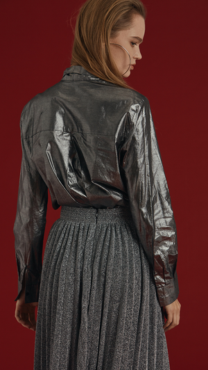 The Blaine is a button-down blouse in glitter sliver metallic. With a self-tied bow, long sleeves. Coated foil.