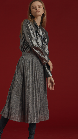 The Blaine is a button-down blouse in glitter sliver metallic. With a self-tied bow, long sleeves. Coated foil.