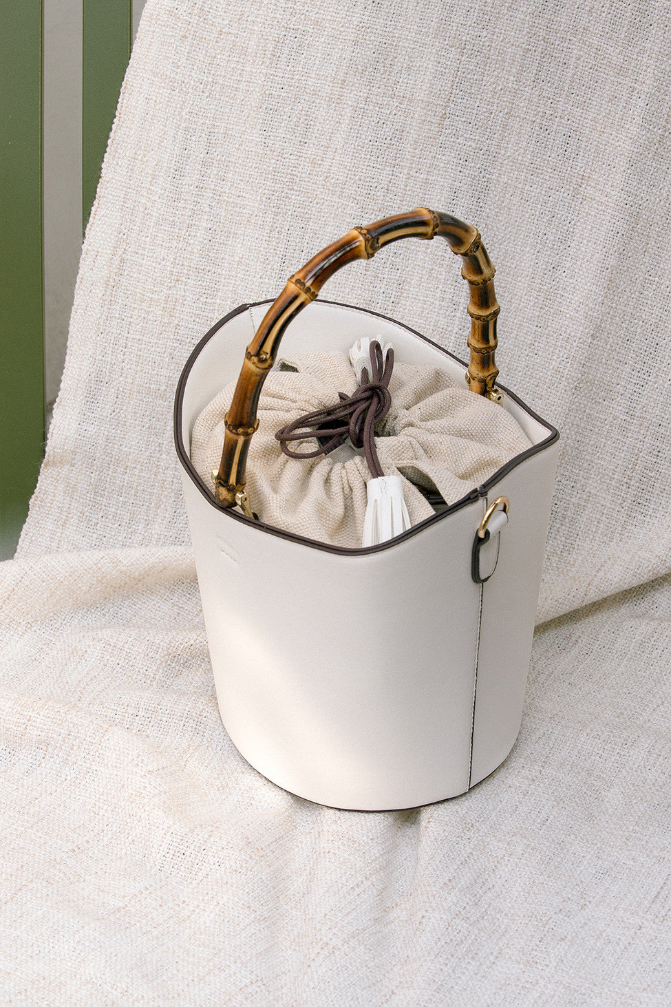 Bonet bag in White. Wooden bamboo carrying top handles. Cylindrical design. Brown drawstring fabric insert with white tassel.