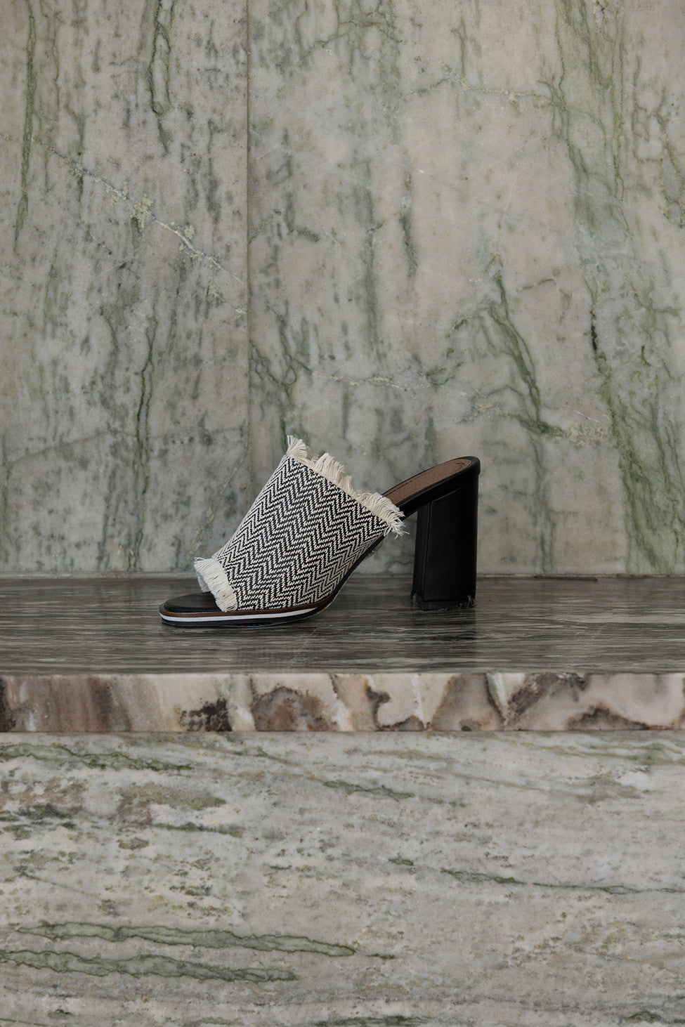 The Brioni sandal in Black-and-White chevron pattern. Open toe. Wool carpet fiber upper with tassel detailing. Slip-on design.