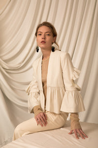 The Cecil Jacket in Ivory, featuring collarless, bracelet sleeves, exaggerated box pleat and open back with ruffle details at elbow. Lightweight.
