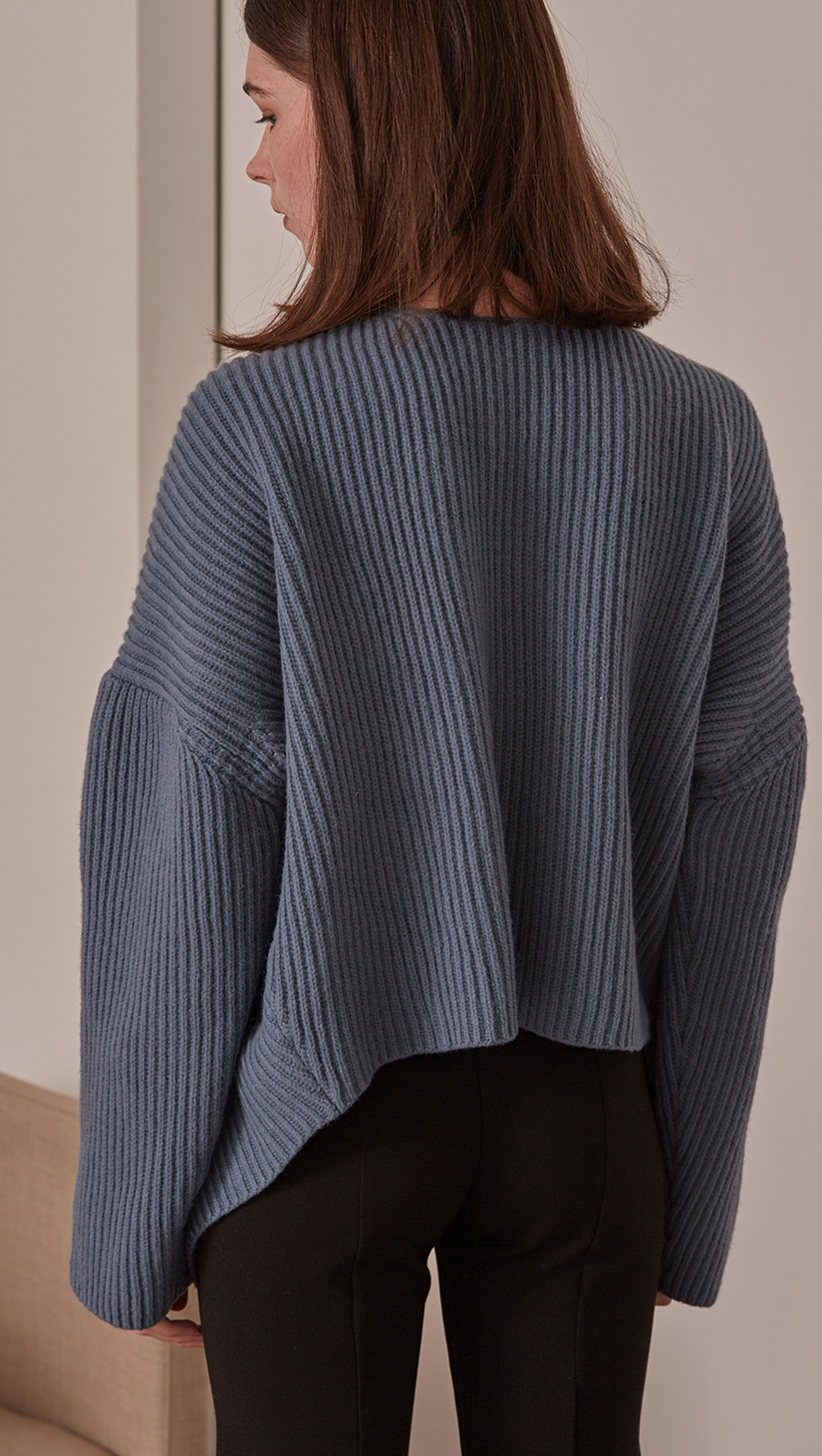 Darah Sweater, a knit sweater in blue. THigh-low length. Twisted opening collar with pointed wide round neckline. Drop shoulder design, open rib details. Short length in open back. Designed to be loose fit.
