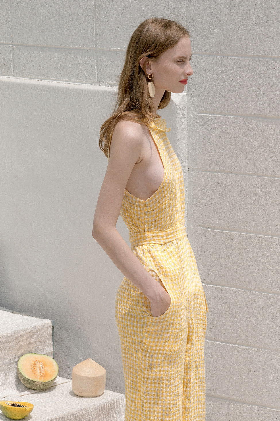 The Ellena jumpsuit in gingham stretchy check fabric with halter neckline. Slanted front pockets. Button closure at back. Detachable self sash belt. Ankle length. Particularly long in length.