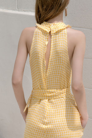 The Ellena jumpsuit in gingham stretchy check fabric with halter neckline. Slanted front pockets. Button closure at back. Detachable self sash belt. Ankle length. Particularly long in length.