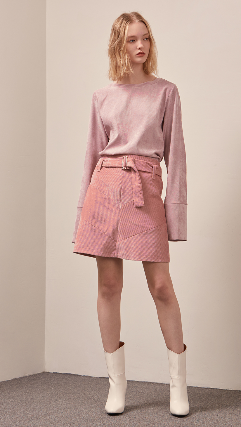 The Ellie Skirt in pink corduroy. With a high-waisted polished A-line style with belt loops. Knee-length skirt.