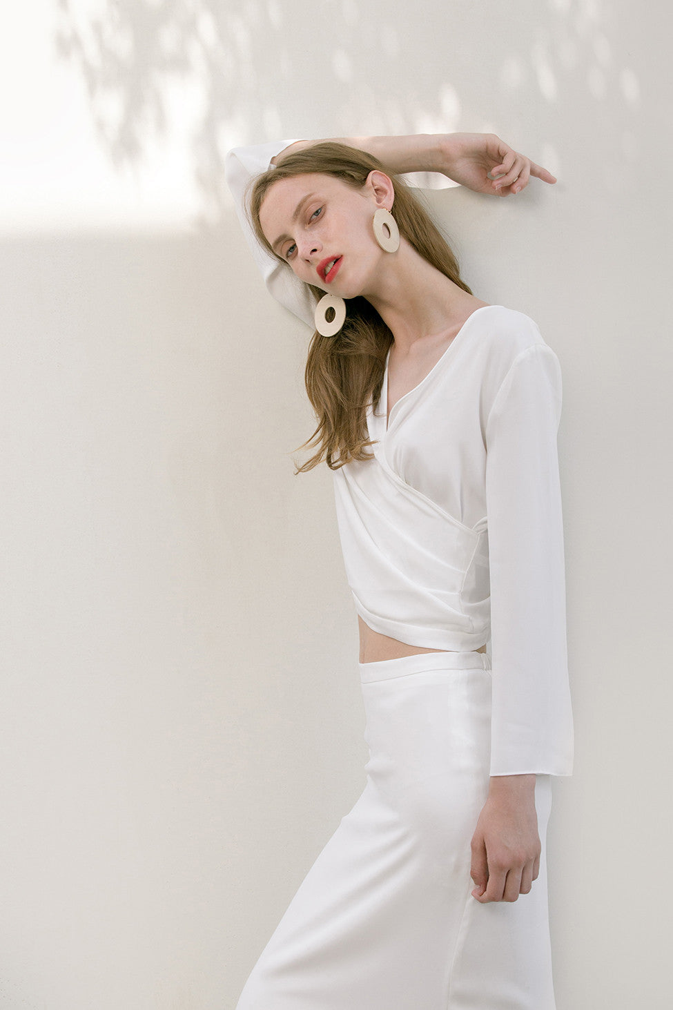 The Emmeline Top in White featuring V-neckline, long sleeves, wrap-front with elasticated band at back hem. Pull on. Lightweight.