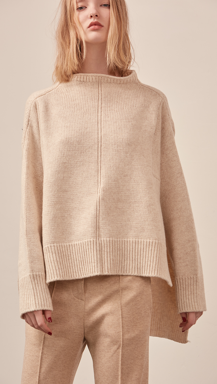 The Erin Sweater in soft oatmeal. Features rolled neckline, long sleeves, drop shoulder, side slits. Pull on. Relaxed silhouette.