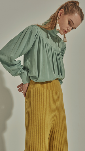 Faé Blouse in Mint. Soft-touch. High turtleneck collar with button closing, button closure at cuff. All-over raglan detailing. Designed to be loose fitting and relaxed. 