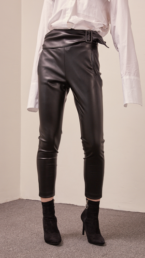 The Gwynn in black stretchy leather pant. Streamlining shape that ends above the ankles, buckled straps at the front, slant two pockets, zipper closing. Slim fit. Starchy Fabric. 