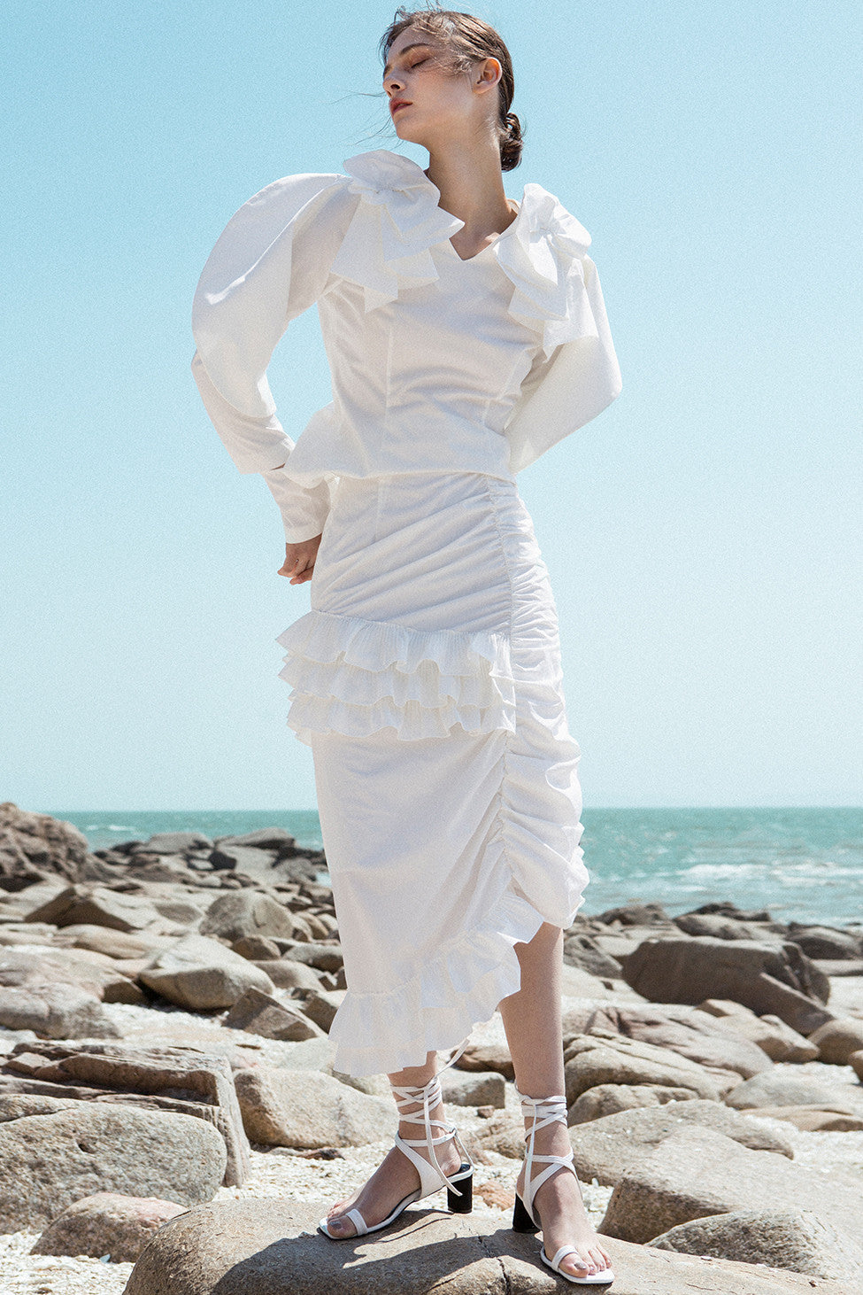 The Aurélie Skirt in White featuring layered ruffles and cut on a bias. Asymmetrical hem. Concelaed side zip closure. Layered ruffles. Partial lined. High rise. 