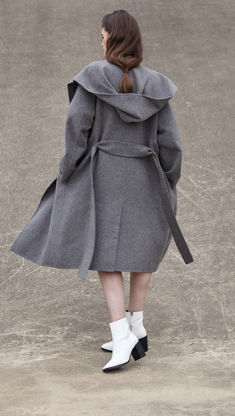 The Handmade Leevia Coat in grey. With a funnel collar, long sleeves, self-tie belt at natural waist. Side seam pockets, wide hoodie, belt loops. Oversized cut. Can be worn open or cinched. 