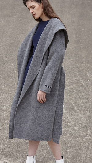 The Handmade Leevia Coat in grey. With a funnel collar, long sleeves, self-tie belt at natural waist. Side seam pockets, wide hoodie, belt loops. Oversized cut. Can be worn open or cinched. 