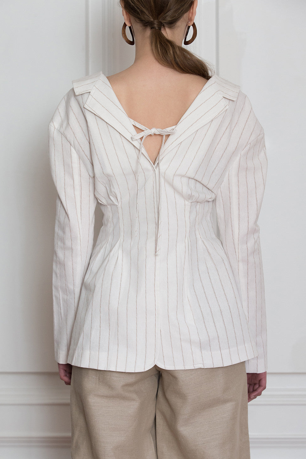 The Souris Jacket in Ivory with brown striped, featuring a-line jacket with fitted waist with one button closure, vertical pleating, open collar with back tie. Fitted at waist.