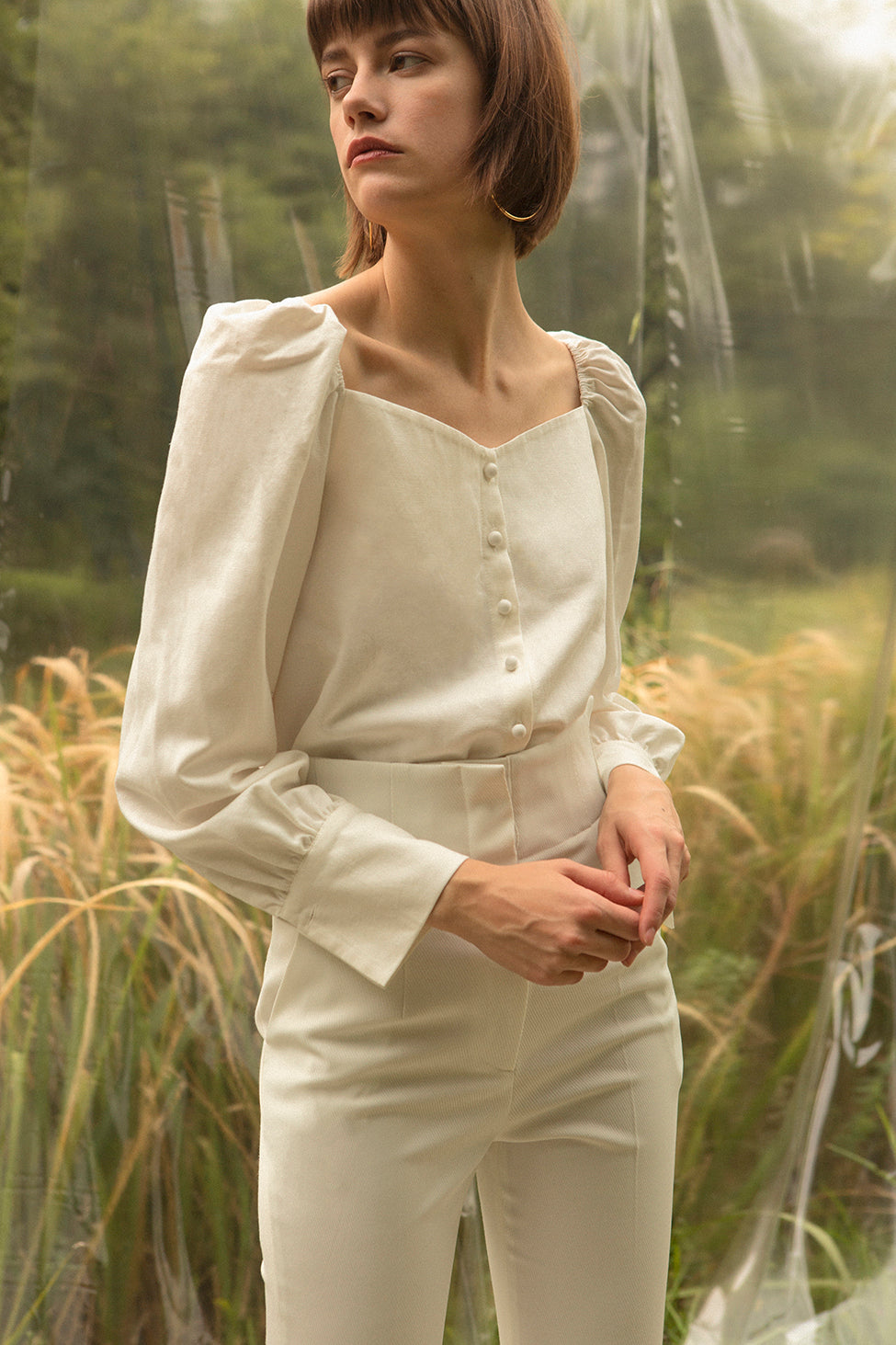 Sculptural blouse in bateau neckline. Ruched details at shoulders. Voluminous sleeves with flounce cuffs and single button closure. Button down closure. Can be styled in off-the-shoulder silhouette.