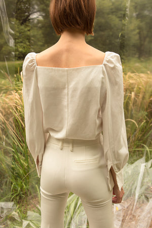Sculptural blouse in bateau neckline. Ruched details at shoulders. Voluminous sleeves with flounce cuffs and single button closure. Button down closure. Can be styled in off-the-shoulder silhouette.