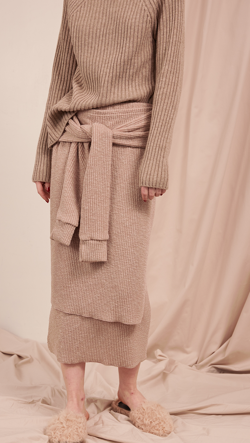 The Natalie Skirt in oatmeal beige. With double layer in ribbed knit, self wrap tie, gathered elastic waistband, deep side slits. Pull on.