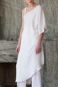 The Rowe Tunic in White. Cut out at one shoulder with D-ring adjustment. Asymmetric hem. Semi sheer. Pull on. 