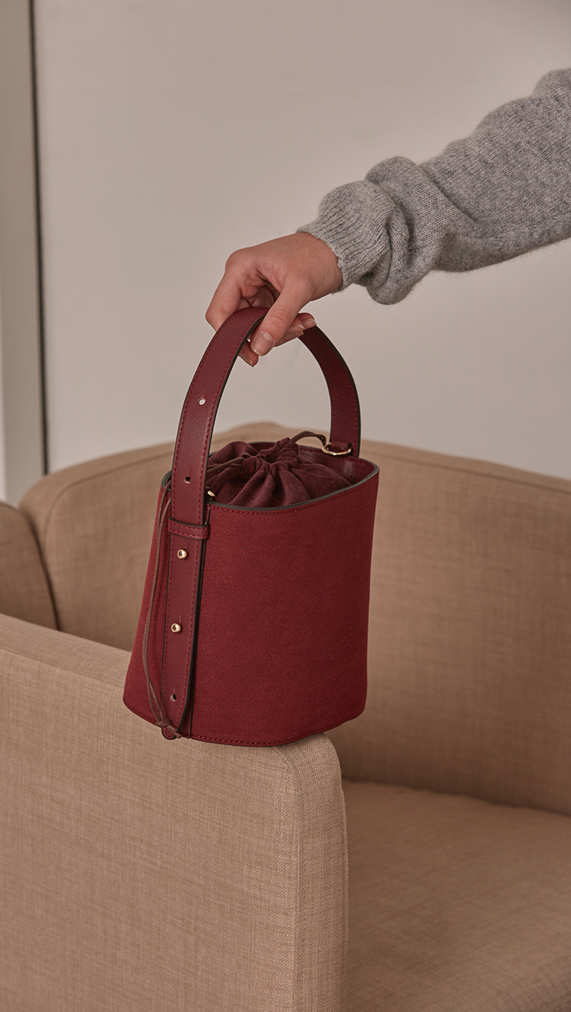 Seed Bucket bag in Burgundy. Main compartment with adjustable strap, detachable shoulder strap, interior pocket with zipper compartment. Structured bottom.