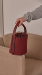 Seed Bucket bag in Burgundy. Main compartment with adjustable strap, detachable shoulder strap, interior pocket with zipper compartment. Structured bottom.