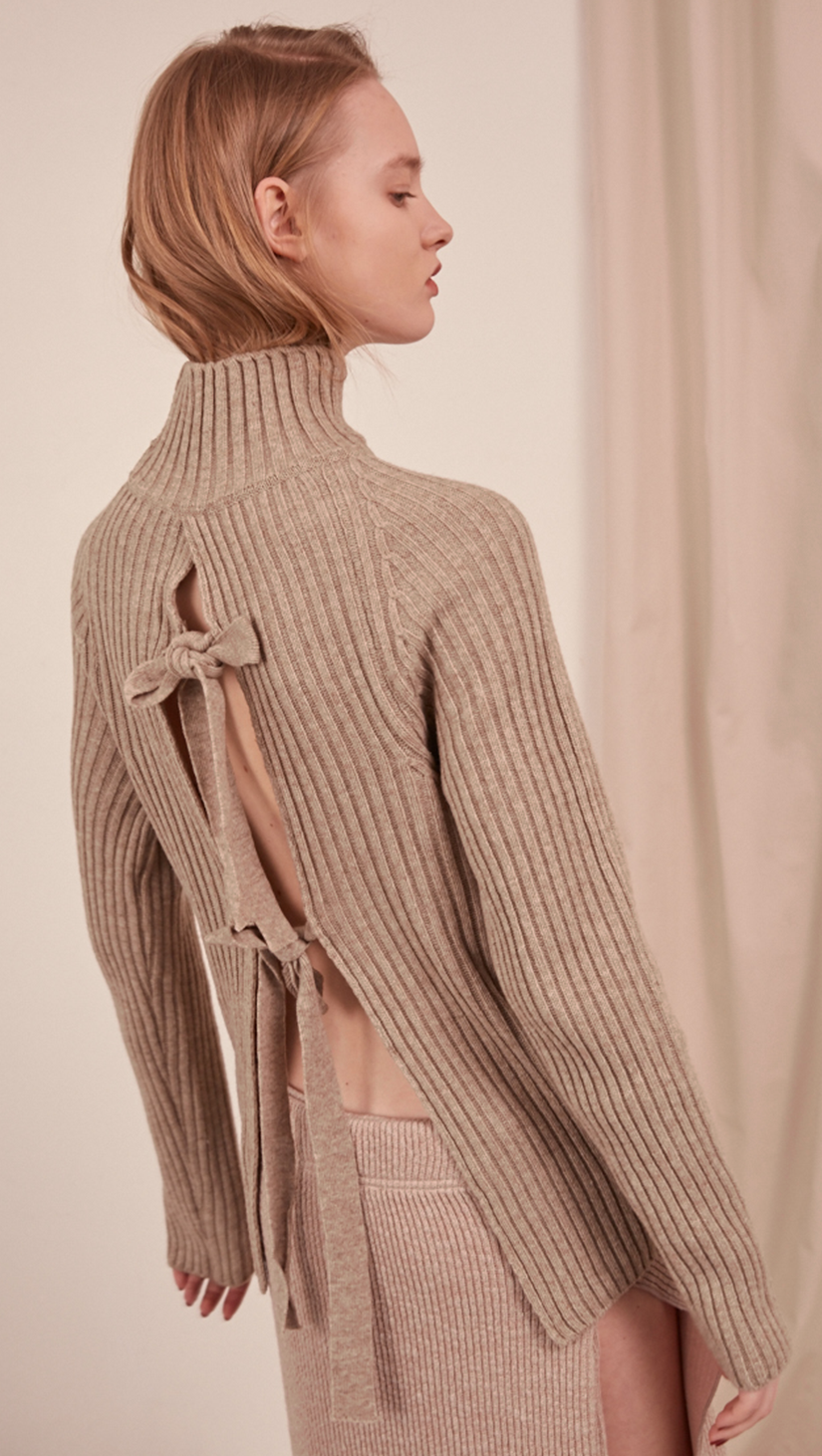 The Simona Knit in oatmeal. Features long sleeve, open back detail in cotton self-tie, ribbed turtleneck. Pull on. Slim fit.