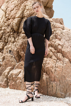 The Soliel Dress in Black, featuring micro-pleated blouse with rounded sleeves, raglan cocoon half sleeves, waistline with drawstring for cinching. Concealed zip down center back. Fitted at waist. Back slits.