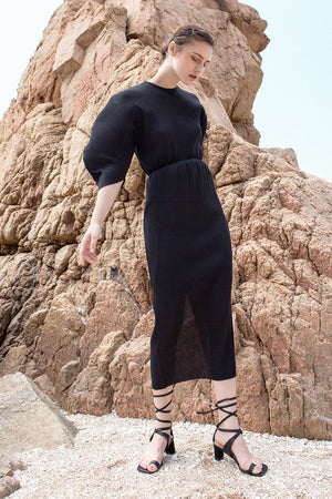 The Soliel Dress in Black, featuring micro-pleated blouse with rounded sleeves, raglan cocoon half sleeves, waistline with drawstring for cinching. Concealed zip down center back. Fitted at waist. Back slits.