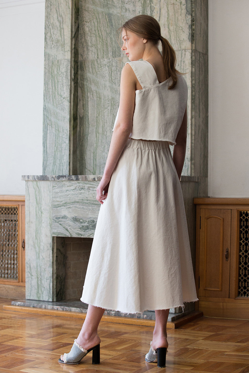 The Sonya set in Off White, top featuring asymmetrical V-neckline, button closure along side. Skirt featuring slant pockets, asymmetrical flare hem in fluted edge, single button fastening with elasticated waistband, high waist in ankle length. Frayed edges.