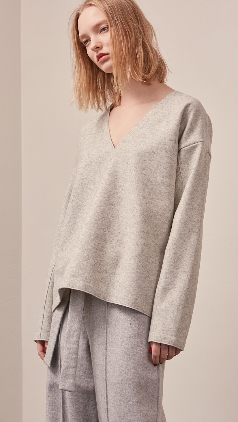 The Stiü wool blend sweater in light grey with a deep V-neckline, long sleeves. Pull on. Lightweight. Non-stretchy. Relaxed fit. 