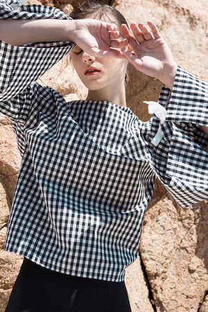 The Tabitha Top in black gingham stripes featuring boat neckline, open-back with drawstring tape back tie. Gathered long wide sleeves. 