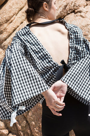 The Tabitha Top in black gingham stripes featuring boat neckline, open-back with drawstring tape back tie. Gathered long wide sleeves. 