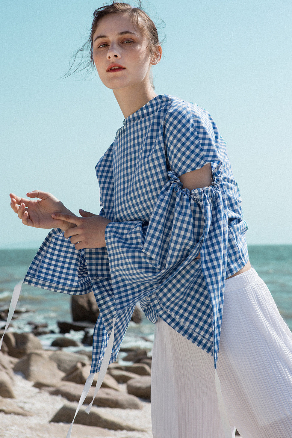 The Tabitha Top in blue gingham stripes featuring boat neckline, open-back with drawstring tape back tie. Gathered long wide sleeves. 