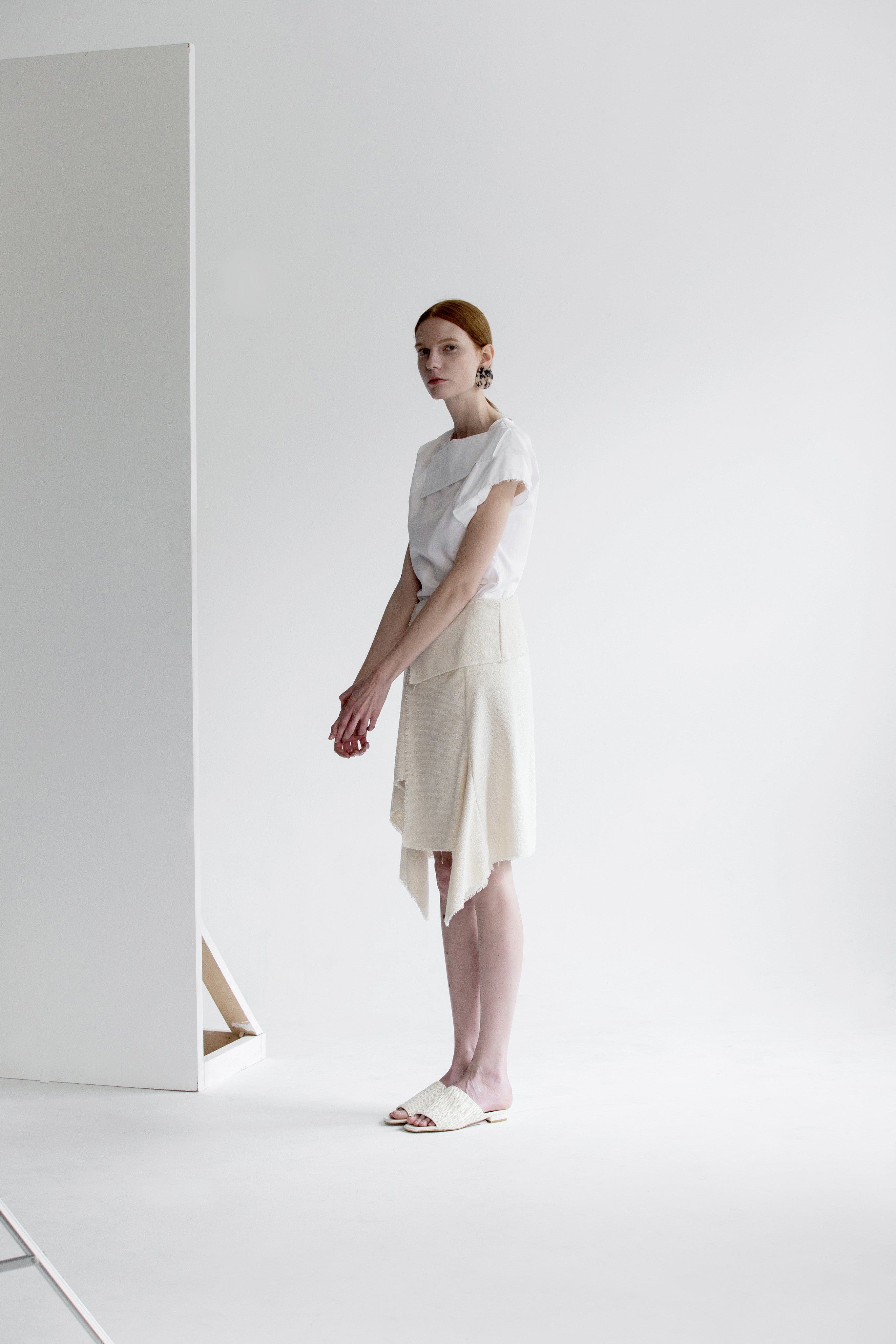 The Vernon Skirt in Ivory featuring cascading ruffle down front. Asymmetrical hem. Wrapover front panel with two snap button. Front vent.